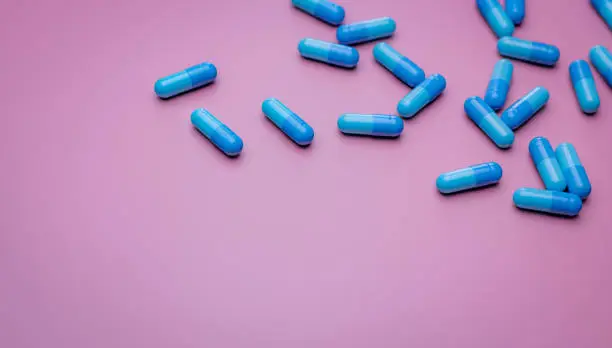 Photo of Top view capsule pills on pink background. Prescription drugs. Blue capsule pills. Pharmaceutical industry. Medicament and pharmacology. Drug development and new drug research. Capsule pills industry.