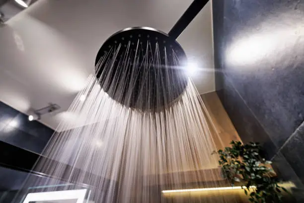 Photo of Water running from a black rain shower head in a dark luxury bathroom