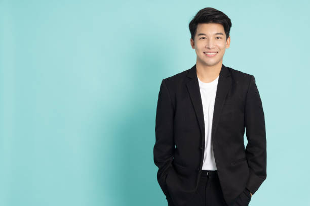 smiling young asian businessman in black suit isolated on green background - businessman business arms crossed business person imagens e fotografias de stock