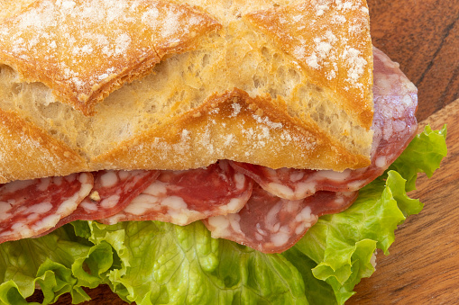 Close-up of a dry sausage sandwich with salad on a wooden background