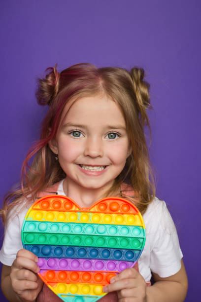 a baby girl holds a popular pop it toy in her hands. a little girl holds a popular pop it toy in her hands. Sensory games for practicing with a neuropsychologist, for people with autism, for the development of fine motor skills Distracted stock pictures, royalty-free photos & images