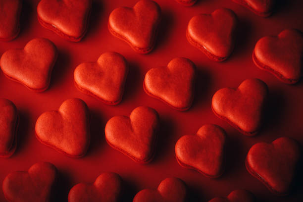 Close-up of heart-shaped red cookies on red background. Pattern made with macaroon cookies with love as a theme. Red toned image.