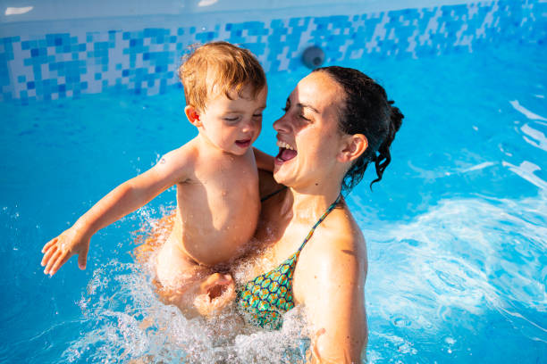 istock Smiling mother holding baby in her arms while playing in a pool 1382131420