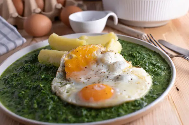 Healthy vegetarian and homemade cooked meal with creamy spinach, fried eggs, sunny side up and boiled potatoes. Served on a plate on wooden table. Ready to eat
