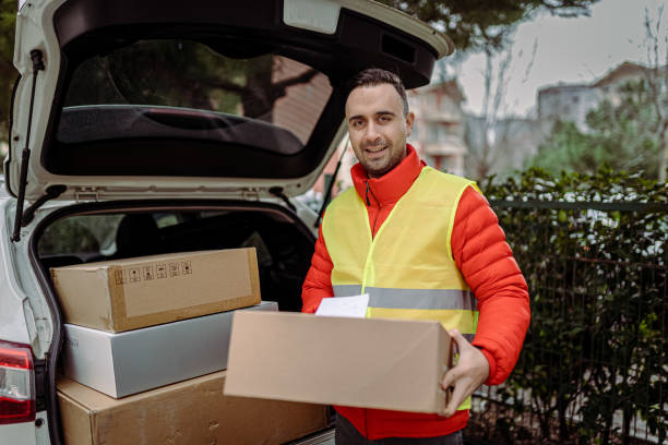 istock Young man courier by a delivery car, carrying parcels. 1382150289
