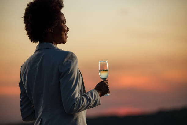 glückliche schwarze geschäftsfrau mit champagner bei sonnenuntergang. - flute solo stock-fotos und bilder