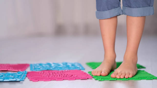 Little boy steps on orthopedic massage mats with different stiffness and texture. Feet Massage Using Trigger Point Spiky Massage Ball. Myofascial Release. close up stock photo