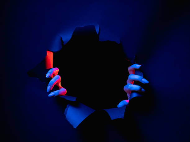 breakthrough background hands ripped wall frame Breakthrough background. Night mystery. Red blue neon light female hands tearing paper ripped wall isolated on dark black round frame empty space. zombie paper stock pictures, royalty-free photos & images