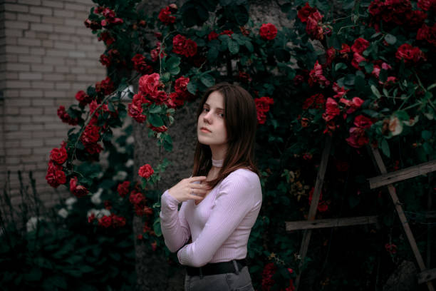 Young girl standing near a bush with red roses.