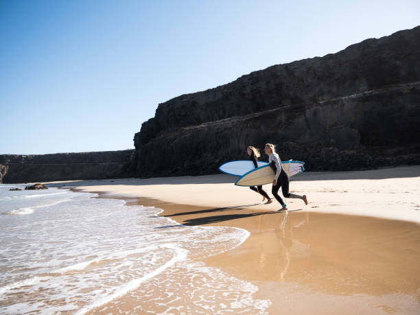 surferinnen rennen zu den wellen - fuerteventura stock-fotos und bilder