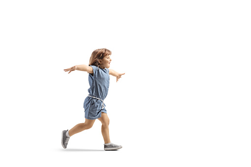 Full length profile shot of a happy little girl running and spreading arms isolated on white background