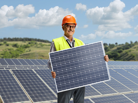 Male engineer with a reflective vest holding a solar panel in a field
