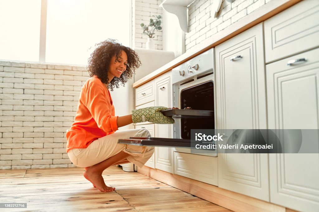 African american family at home African American cute woman with curly fluffy hair taking out a baking sheet with baked muffins from the oven. Oven Stock Photo