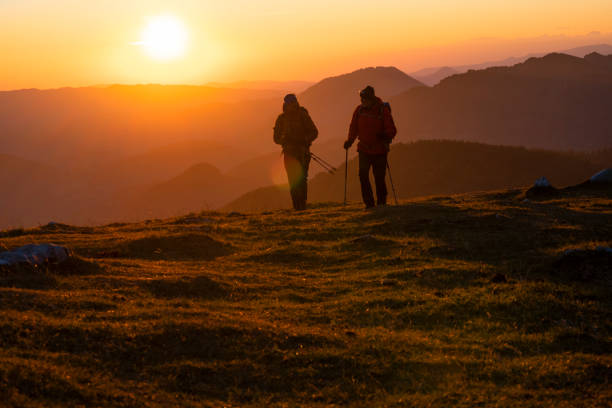 Rear view of male hikers with rucksacks and hiking poles walking on top of mountain.