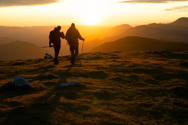 Rear view of male hikers with rucksacks and hiking poles walking on top of mountain.