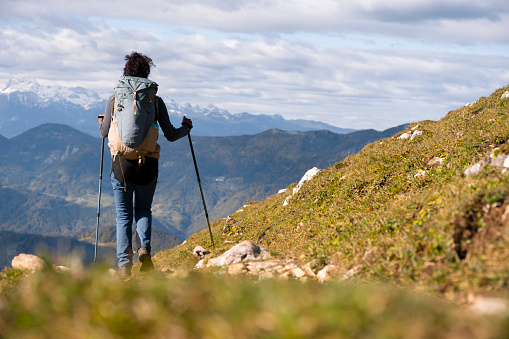 Rear view of mature woman hiking with hiking poles on mountain against cloudy sky.