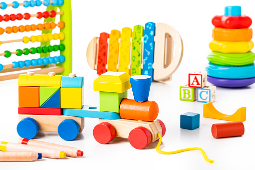 Front view of a group of educational toys against white background. The composition includes a wooden train, some crayons, an abacus, a xylophone, some wooden blocks with the letters A B C, and a multicolored pyramid.