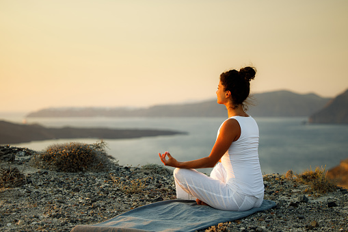 Relaxed woman doing Yoga meditation exercises in Lotus position on a hill above the sea. Copy space.