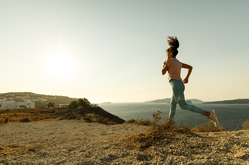 Young female athlete jogging on a hill during summer day above the sea. Copy space.