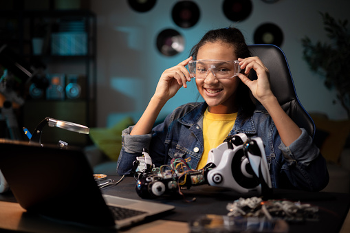 Girl soldered cables, electronic wires, pulls safety goggles, fixes broken robot