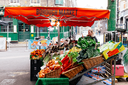 London, UK - 4 March, 2022: color image depicting a market stall workers in Borough Market, London, UK. The stalls are selling a variety of fresh fruit and vegetables. Borough Market is one of the oldest and most popular food markets in the UK and globally. Colour image with copy space.