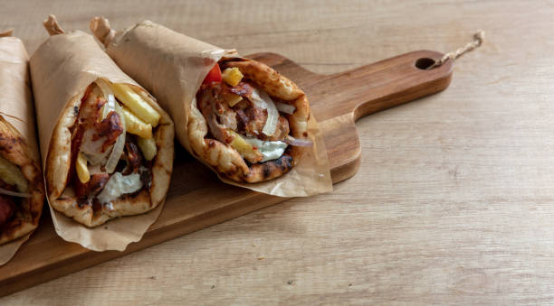 gyro pita shawarma wrap on wood table. greek food with slice cut meat, overhead - souvlaki imagens e fotografias de stock
