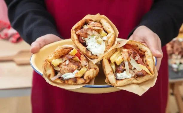 Gyro pita Shawarma.  Greek food, sliced meat, potato, tomato and tzatziki, paper wrap served in a plate, close up view.