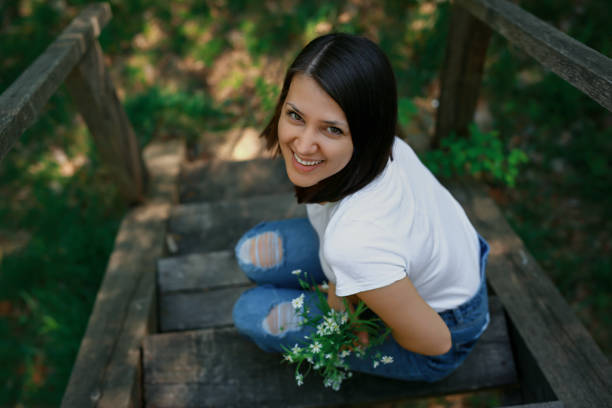 A laughing woman is sitting in the park on the old wooden stairs with a bouquet of white wild flowers.