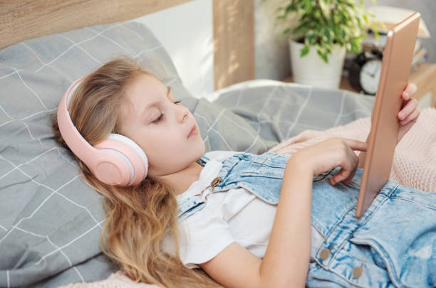 istock Cute Little girl lying on bed and using tablet at home 1382251101