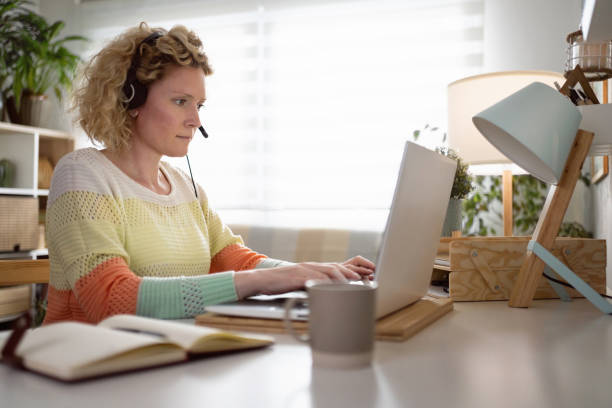From home office, female dispatcher working while using headset and laptop stock photo