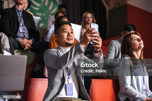 istock Young well dressed man taking a photo while attending business conference 1382270368