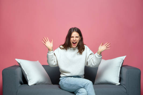 istock Nervous irritated young girl spreading hands shouting what, sitting on sofa. Misunderstanding, quarrel, conflict 1382270464
