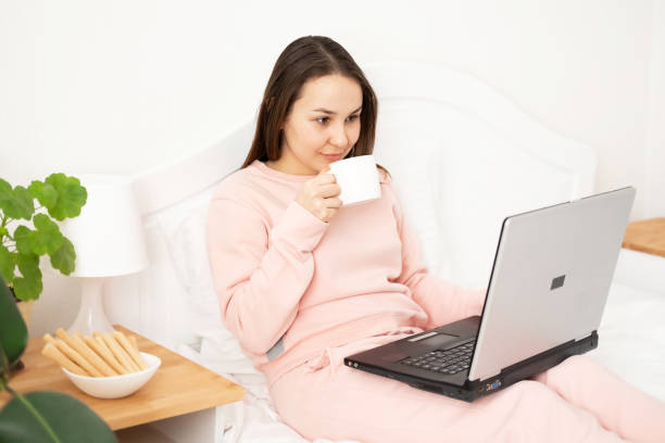 istock Woman girl using laptop working office work remotely from home sitting on bed with tea cup. Distance learning online education and work, video communication. 1382271806