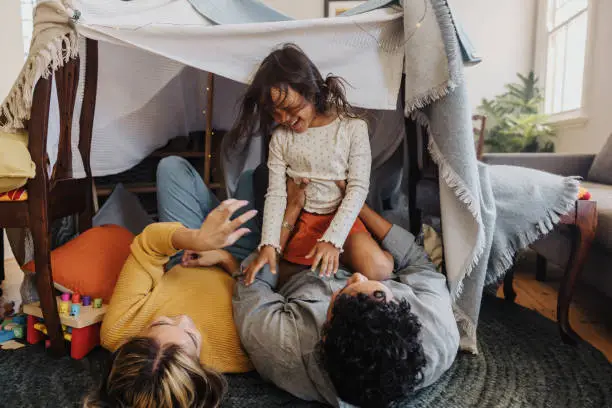 Photo of Happy little girl playing with her mom and dad at home