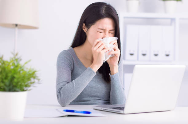 Stressed young  woman sneezing  and working at home office stock photo