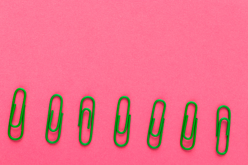 Colored paper clips. Green paper clips macro close up isolated on a pink background with copy space.