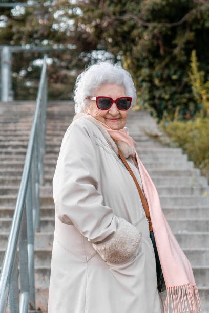An elegantly dressed older lady posing on some stairs in the city streets