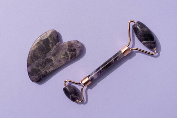 istock Facial massage kit - amethyst gua sha tool and face roller on trendy purple background. Face roller, massager made from natural stones. Skin care routine 1382276862