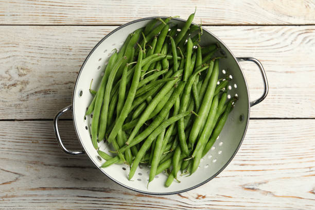 istock Fresh green beans in colander on white wooden table, top view 1382284101