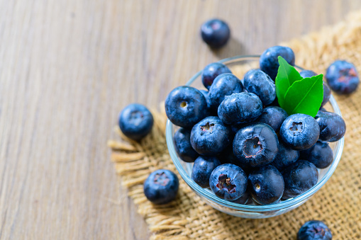 Fresh organic blueberries in a glass bowl on wood background, top view, Healthy fruits
