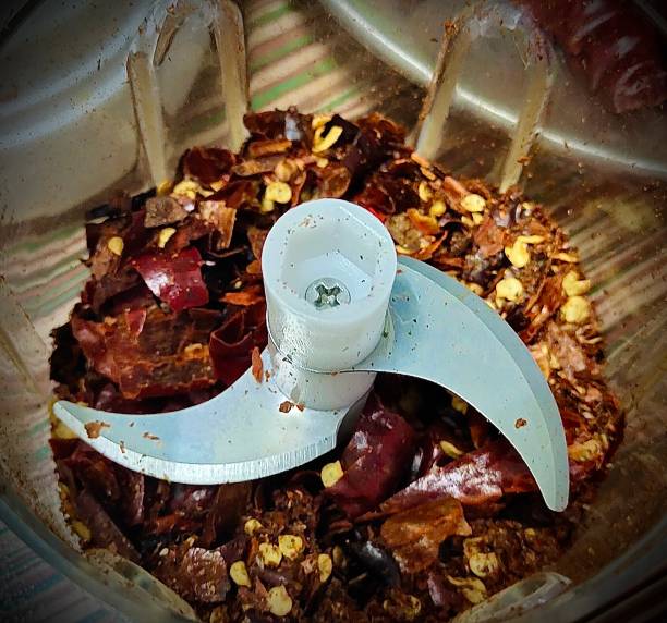Close-up view of various kinds of pepper in stone mortar. Grinding pepper in mortar with pestle. Several peppercorns falling out from mortar.