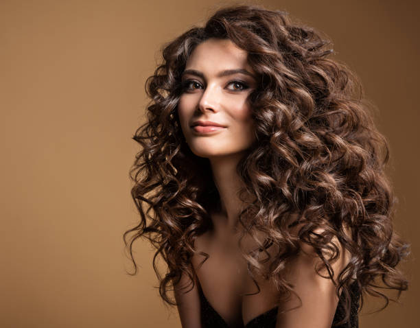 modello di capelli ricci. donna ondulata acconciatura lunga. brunette fashion girl con volume hairdo e trucco naturale su sfondo beige - beautiful hair foto e immagini stock