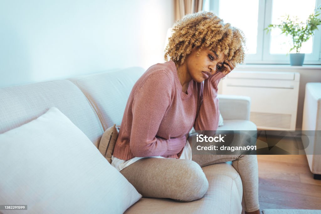 Woman with menstrual pain Woman lying on sofa looking sick in the living room. Beautiful young woman lying on bed and holding hands on her stomach. Woman having painful stomachache on bed, Menstrual period Pain Stock Photo
