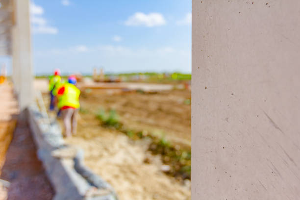 Clouse-up view on beam, pilar of unfinished concrete edifice. People are working in background with safety vests and helmets.