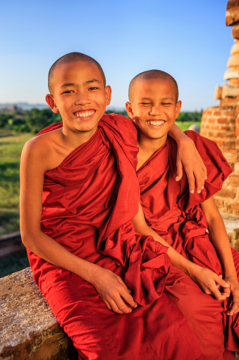Young Buddhist monk sitting together and admiring view of ancient temples in Bagan, Myanmar (Burma)