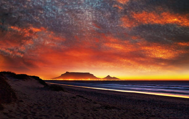 espectacular vista crepuscular de table mountain, ciudad del cabo, sudáfrica a través de table bay con la ciudad y el cielo en llamas de luz - montaña de lions head fotografías e imágenes de stock