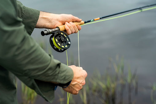 Close-up of a man holding fishing rod while doing fly fishing in a pond