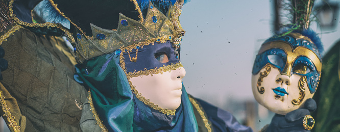 Attractive masked person posing in front of house building at one of numbered canals in Venice, Italy.