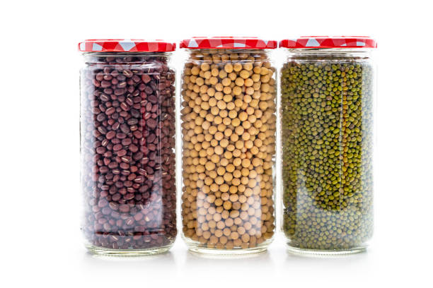 Assorted soybeans soy beans legumes in glass jar in a row on white background as: white soybean, mung bean and adzuki bean