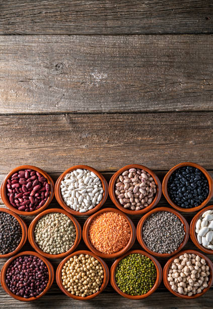 Assorted legumes in round clay containers on rustic wooden background leaving copy space including lentils, chickpeas,soybeans and beans
